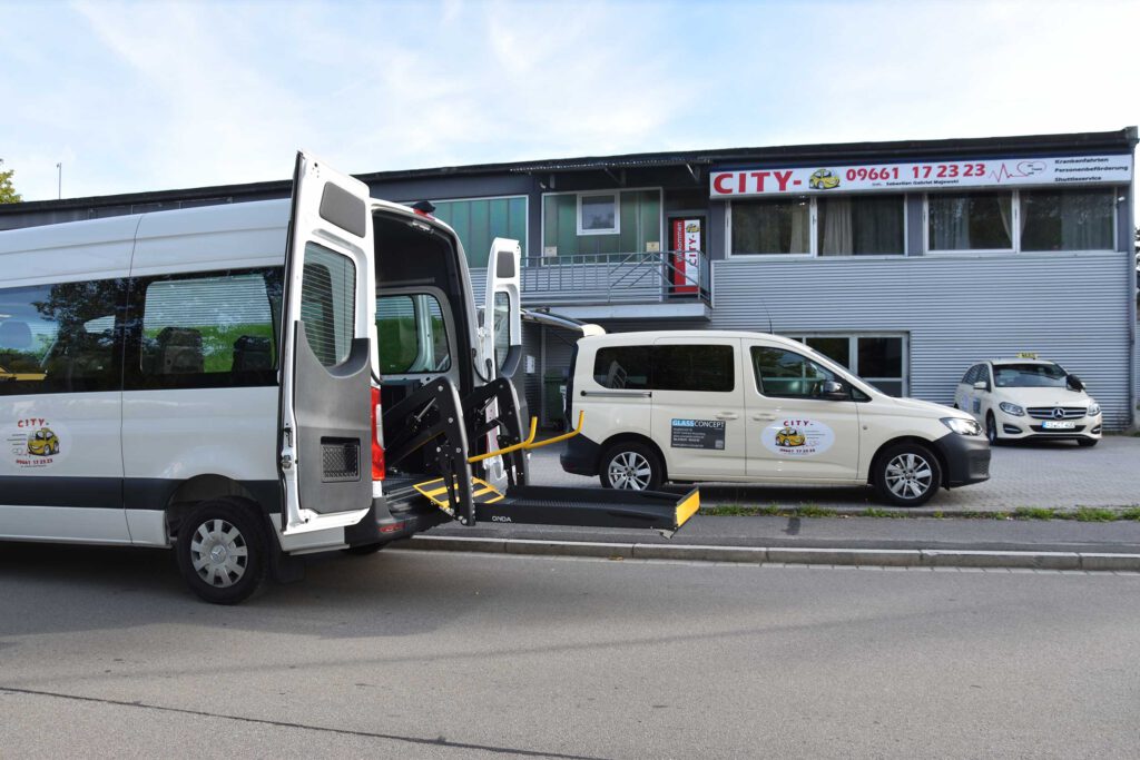 Fahrzeugflotte von City-Taxi vor dem Firmengebäude, im Vordergrund ein Mercedes-Benz Sprinter mit ausgefahrener Rollstuhlrampe